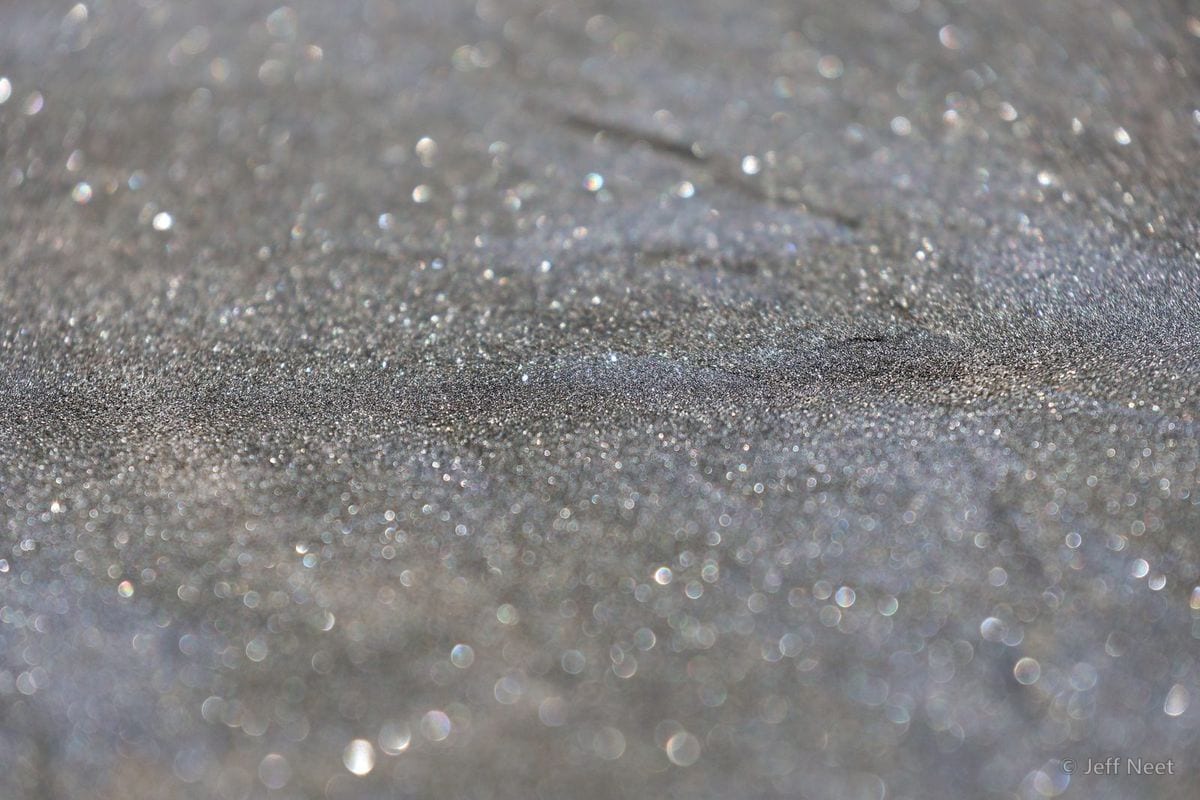 Close view of sand grains sparkling with small points of light across a soft grey surface.
