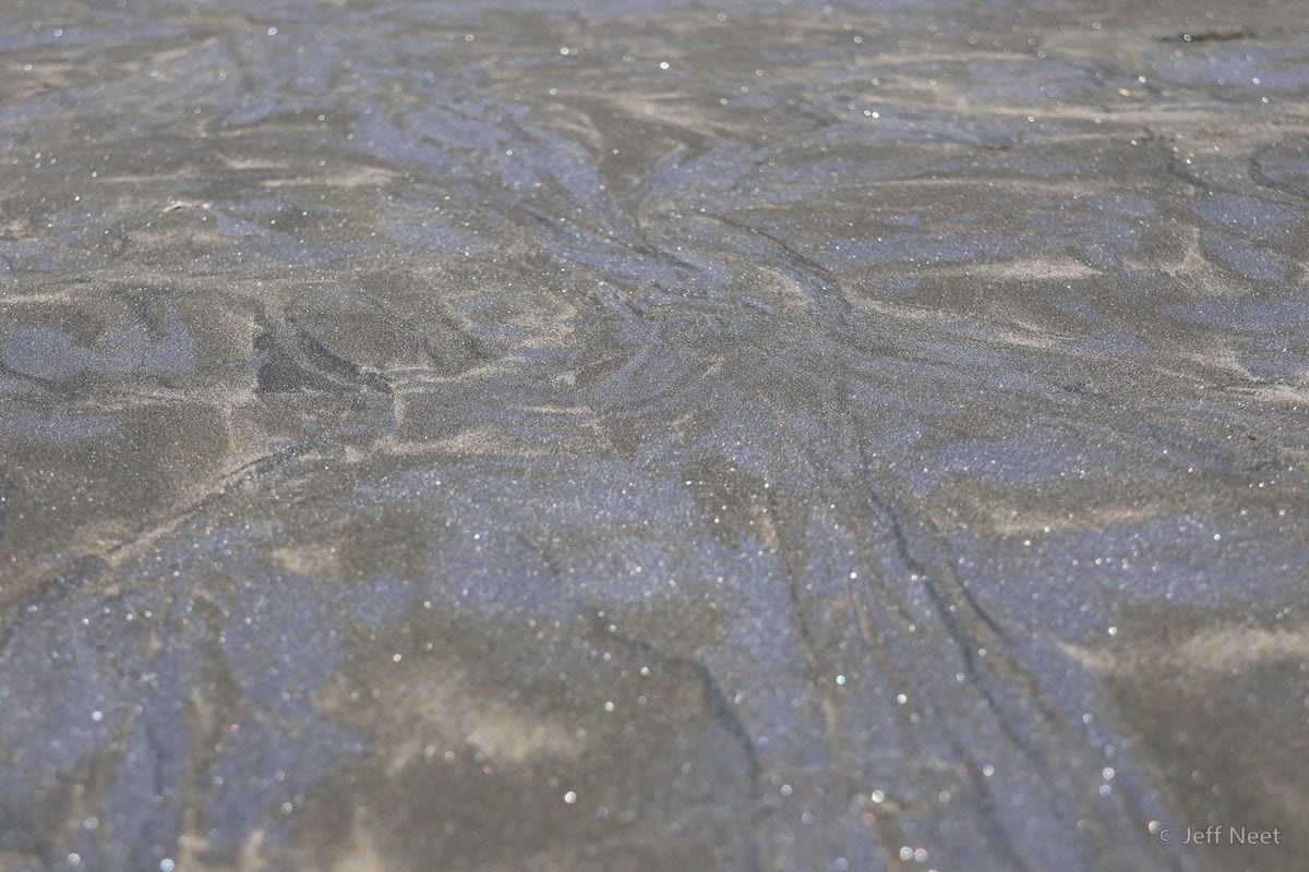 Grey-blue wet sand with ripple lines and tiny glints of light across its surface.